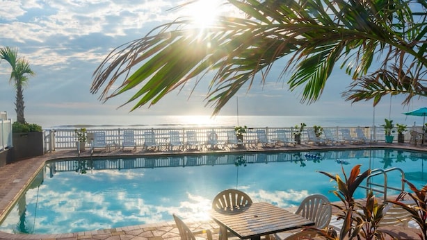 A pool area with a view of the sea, lounge chairs, and a table with chairs. - Boardwalk Inn and Suites (Daytona Beach)