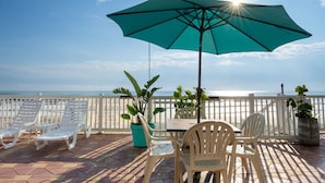 A terrace with lounge chairs, a table, and a large umbrella overlooking the ocean. - Boardwalk Inn and Suites (Daytona Beach)