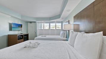 A hotel room with two beds, a TV, a desk, and a window with blinds.