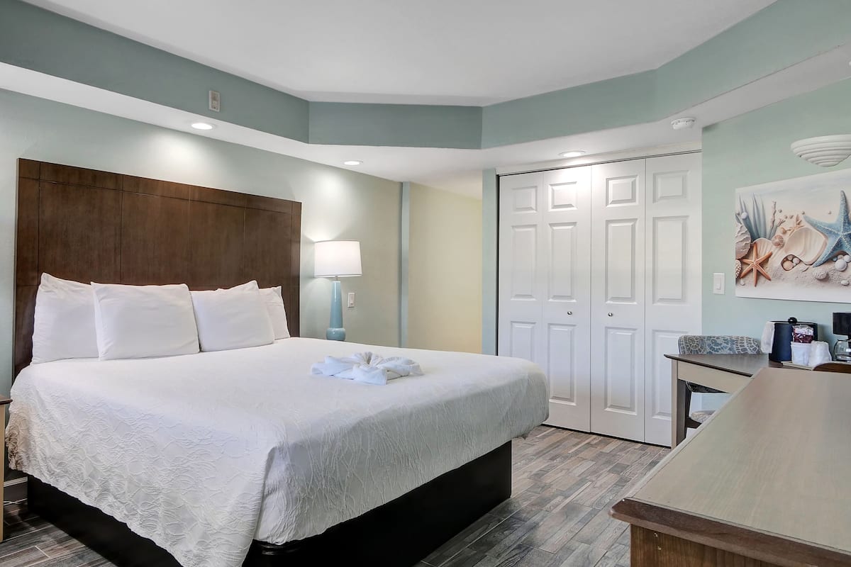 A neatly arranged hotel room with a large bed, two bedside lamps, a wooden headboard, a white door, and a small table with a lamp.