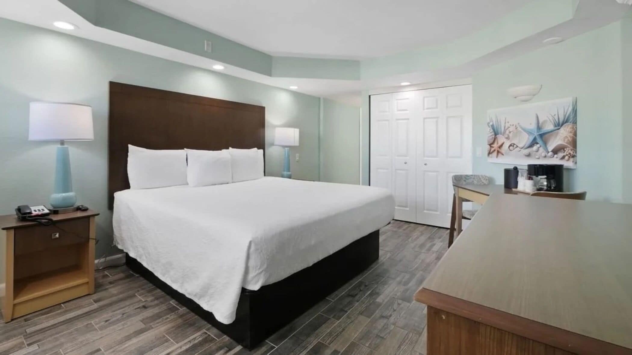 A hotel room with a large bed, a desk, a chair, a lamp, a phone, and a coffee maker.