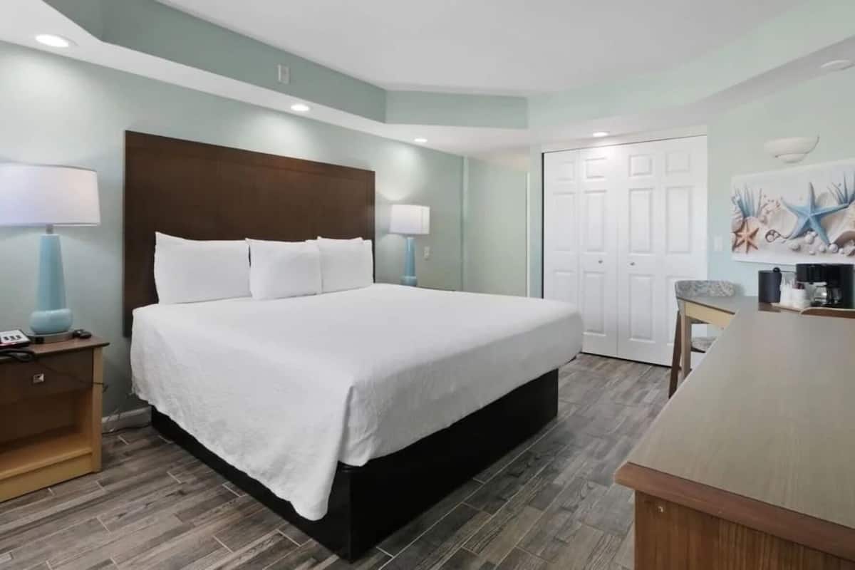 A hotel room with a large bed, a desk, a chair, a lamp, a phone, and a coffee maker.