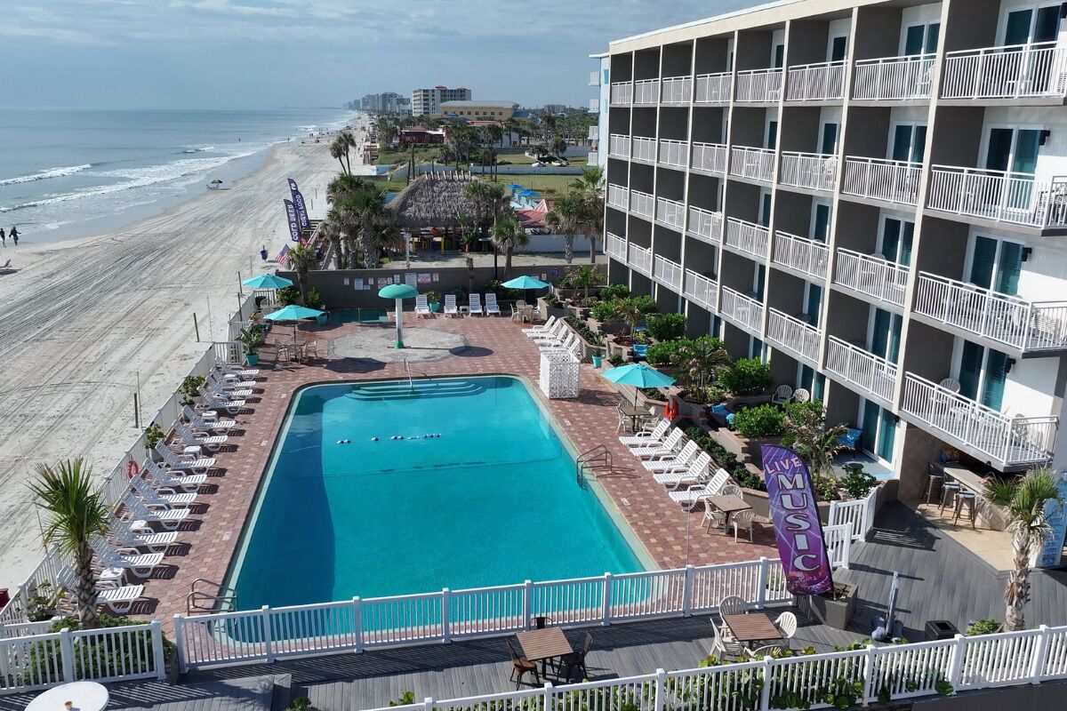 A hotel with a pool, beach view, and outdoor seating area.