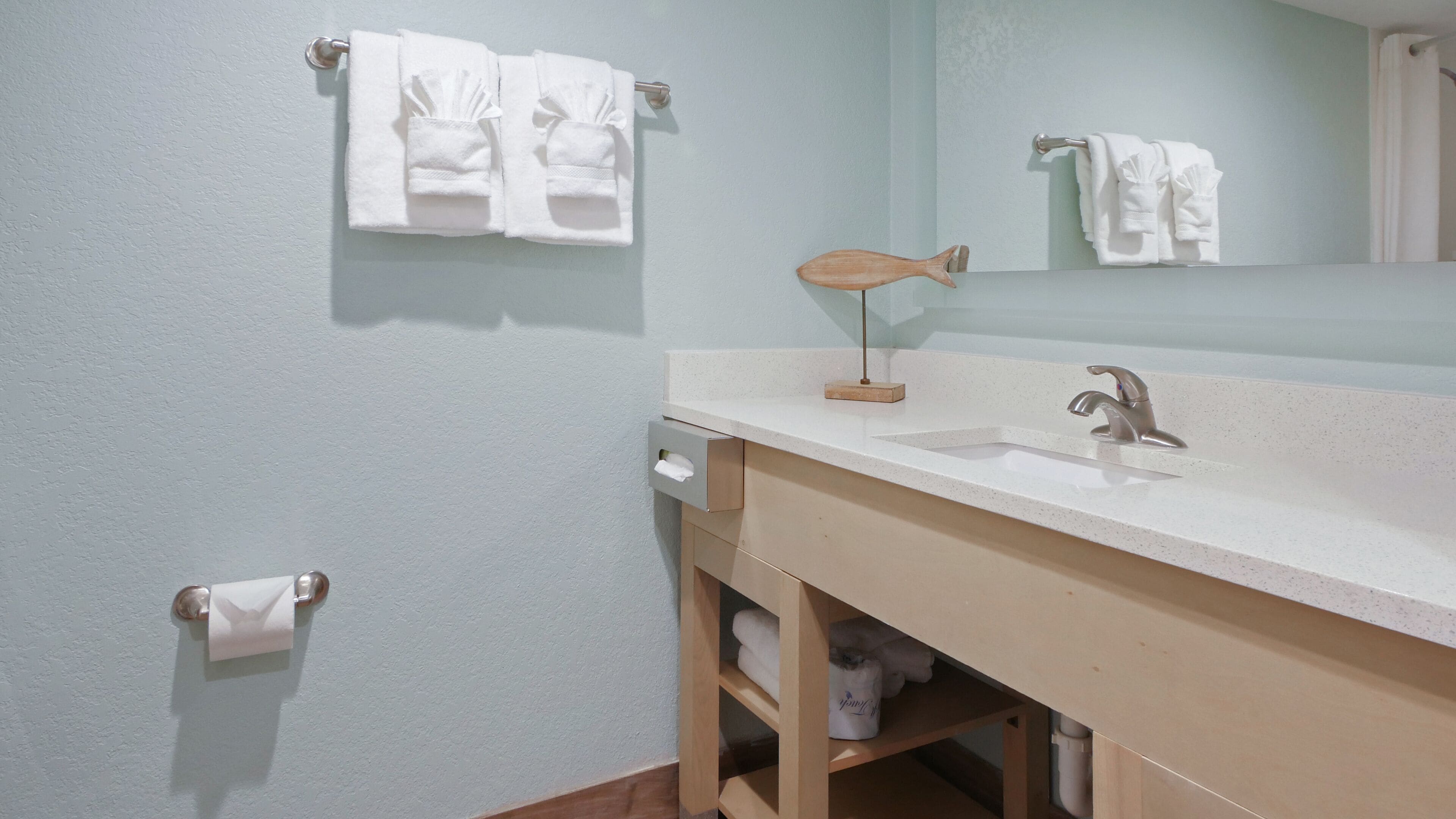 A bathroom with a sink, mirror, towel rack, and a wooden shelf under the sink.