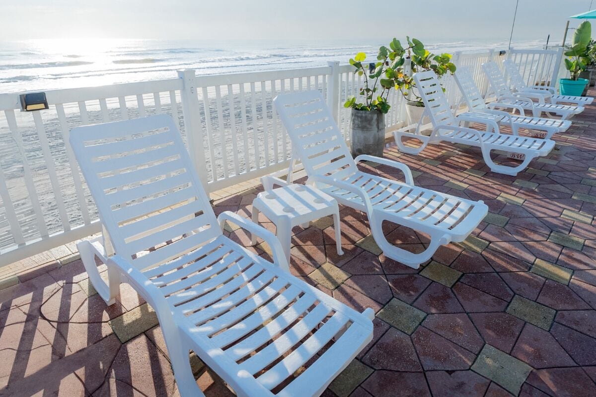 A series of white lounge chairs arranged on a tiled deck with a view of the ocean.