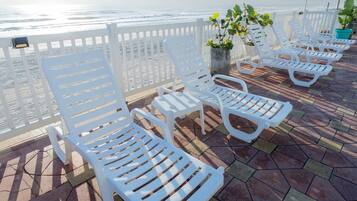 A series of white lounge chairs arranged on a tiled deck with a view of the ocean.
