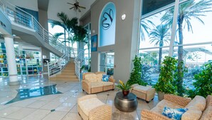 A spacious lobby with a staircase, wicker furniture, and large windows overlooking palm trees. - Boardwalk Inn and Suites (Daytona Beach)