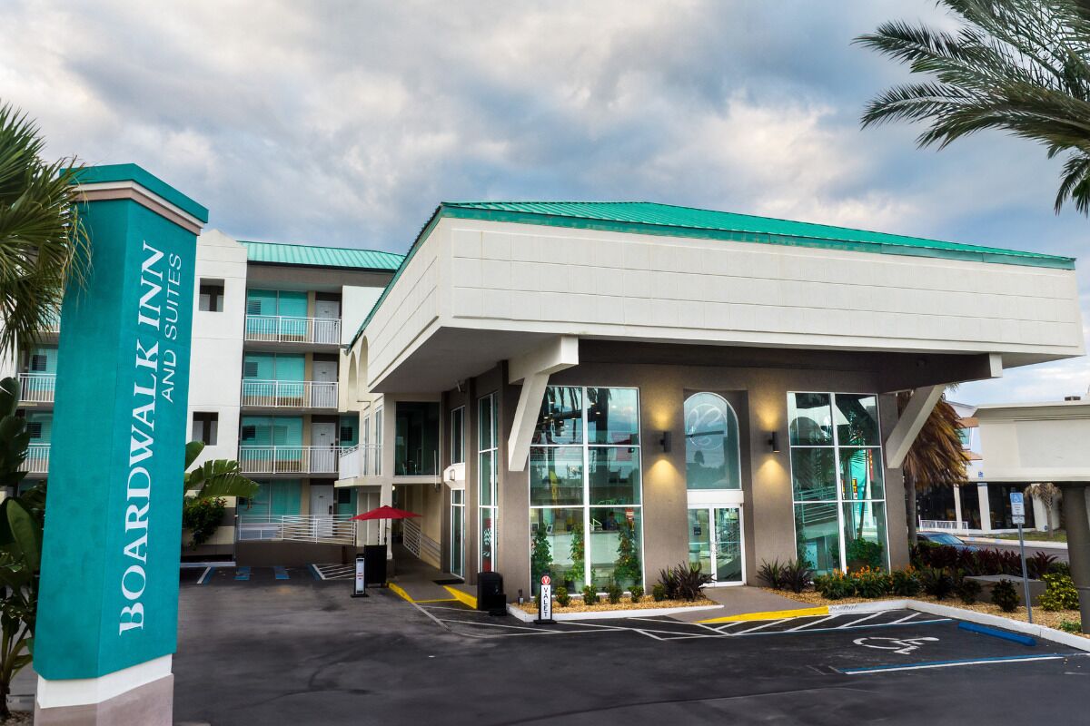 A Boardwalk Inn with a modern design, featuring a large entrance canopy, a parking area with handicapped accessibility, and a multi-story building with balconies.