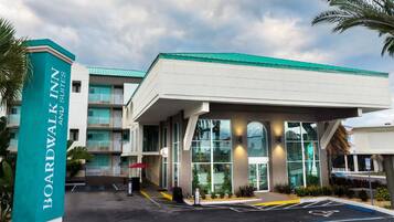 A Boardwalk Inn with a modern design, featuring a large entrance canopy, a parking area with handicapped accessibility, and a multi-story building with balconies.