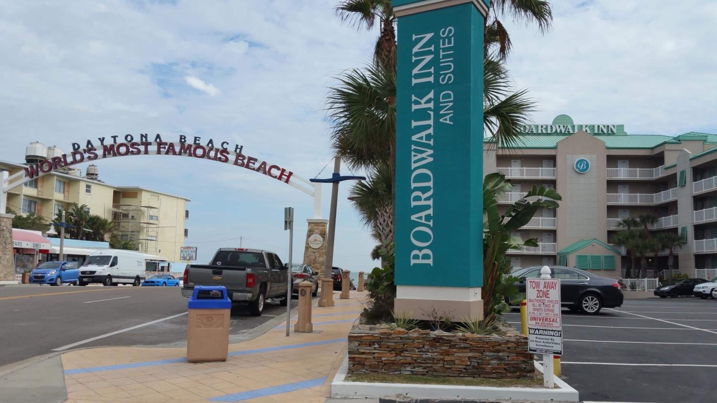 A sign for Boardwalk Inn and Suites with a view of Daytona Beach's famous beach in the background.