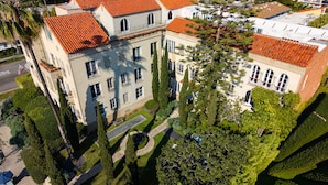 A large, multi-story building with a red-tiled roof, surrounded by well-maintained greenery and other buildings. - Maison Twenty Seven (Santa Monica)