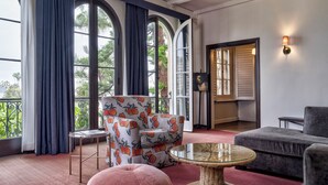 A spacious room with large windows, a round wicker table, a grey sofa, and a patterned armchair. - Maison Twenty Seven (Santa Monica)