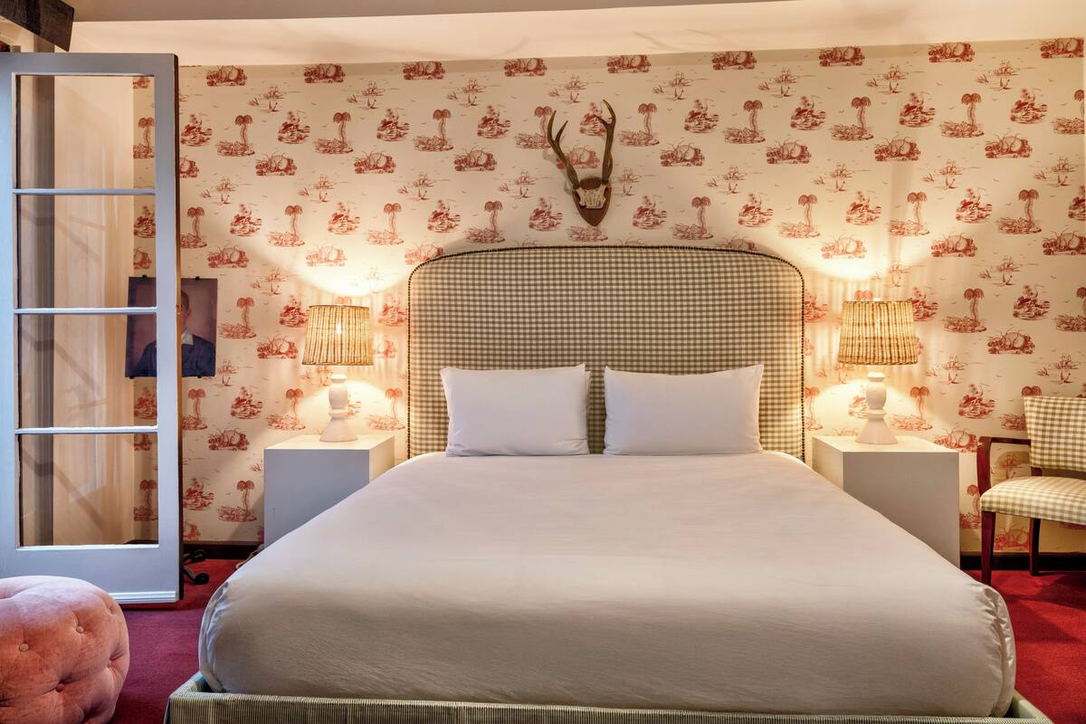 A neatly arranged bedroom with a large bed, two bedside tables with lamps, a chair, and a mirror.