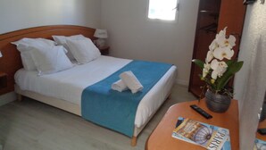 Une chambre d’hôtel avec un lit, une table de chevet, une armoire, une fenêtre et un magazine sur une table.