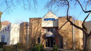 Un hôtel à la façade en briques, avec une enseigne indiquant « HÔTEL », et une petite entrée avec un chemin menant à la porte.