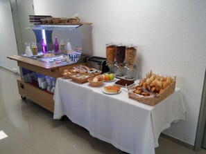 Un buffet proposant une variété de plats et de boissons, notamment du pain, des pâtisseries et des condiments.