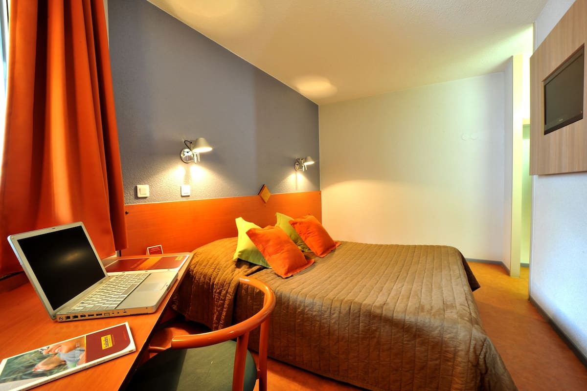A hotel room with a bed, a desk with a laptop, and a chair.