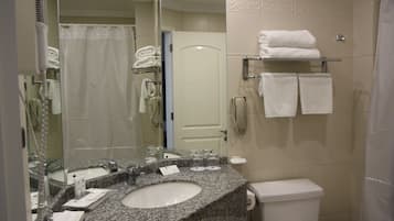 A bathroom with a granite sink, a white toilet, a glass shower enclosure, and a towel rack with folded towels.