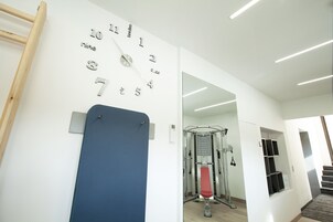 A modern room with a wall-mounted clock, a pull-up bar, and a gym area with a bench press and cable machine.