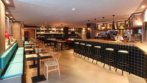 A modern bar area with a long counter, stools, and a variety of bottles and glasses.