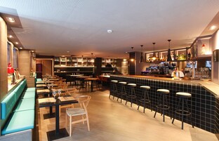 A modern bar area with a long counter, stools, and a variety of bottles and glasses.
