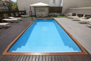 A rectangular pool with a wooden deck surrounding it, a white canopy, and lounge chairs. - Hotel Concordia (Barcelona)