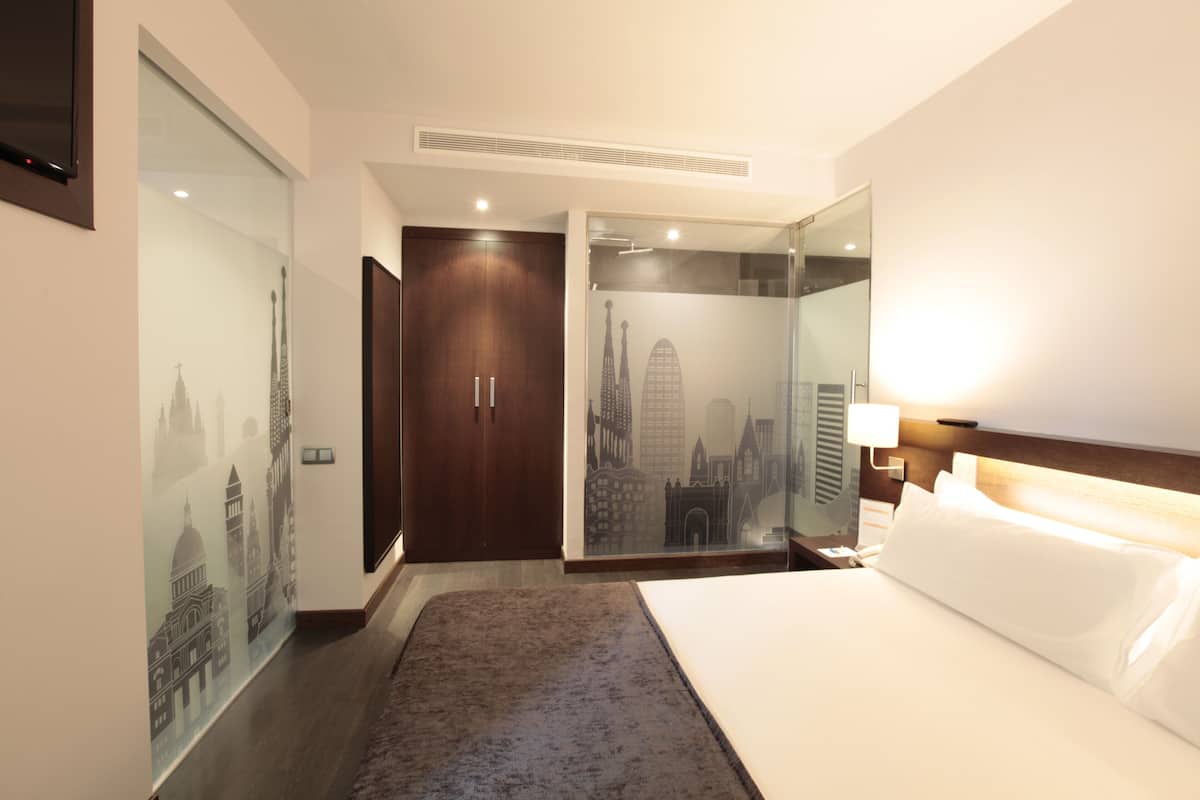 A hotel room with a bed, a nightstand, a mirror, a door, and a wall with a cityscape mural.