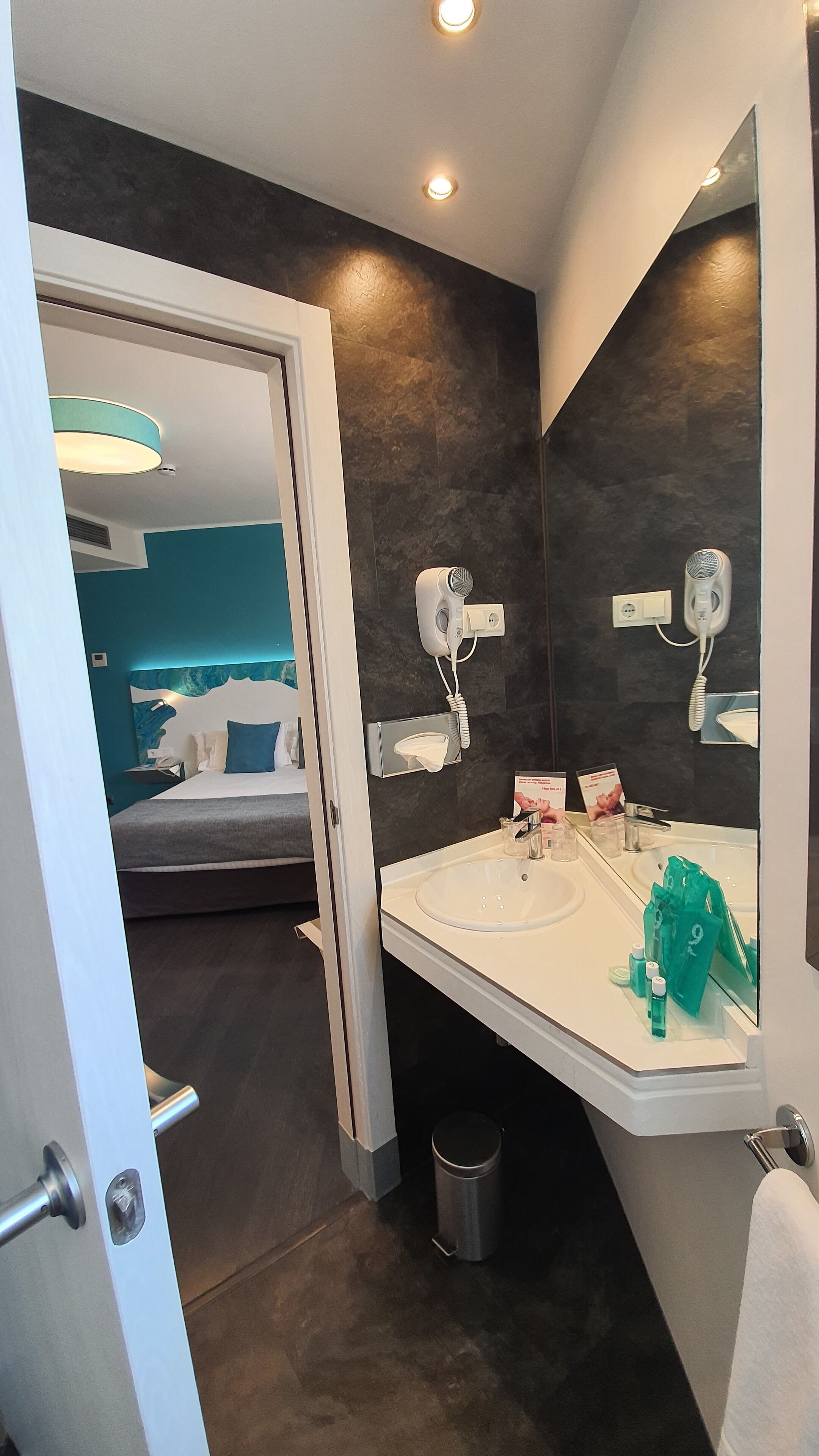 Un baño moderno con un espejo grande, dos secadores de pelo, un lavamanos y un cubo de basura.