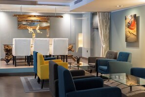 A modern lounge area with a glass table, blue and yellow chairs, and a wooden sculpture centerpiece. - Hotel Concordia (Barcelona)