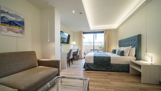 A modern hotel room with a bed, a sofa, a desk, and a TV.
