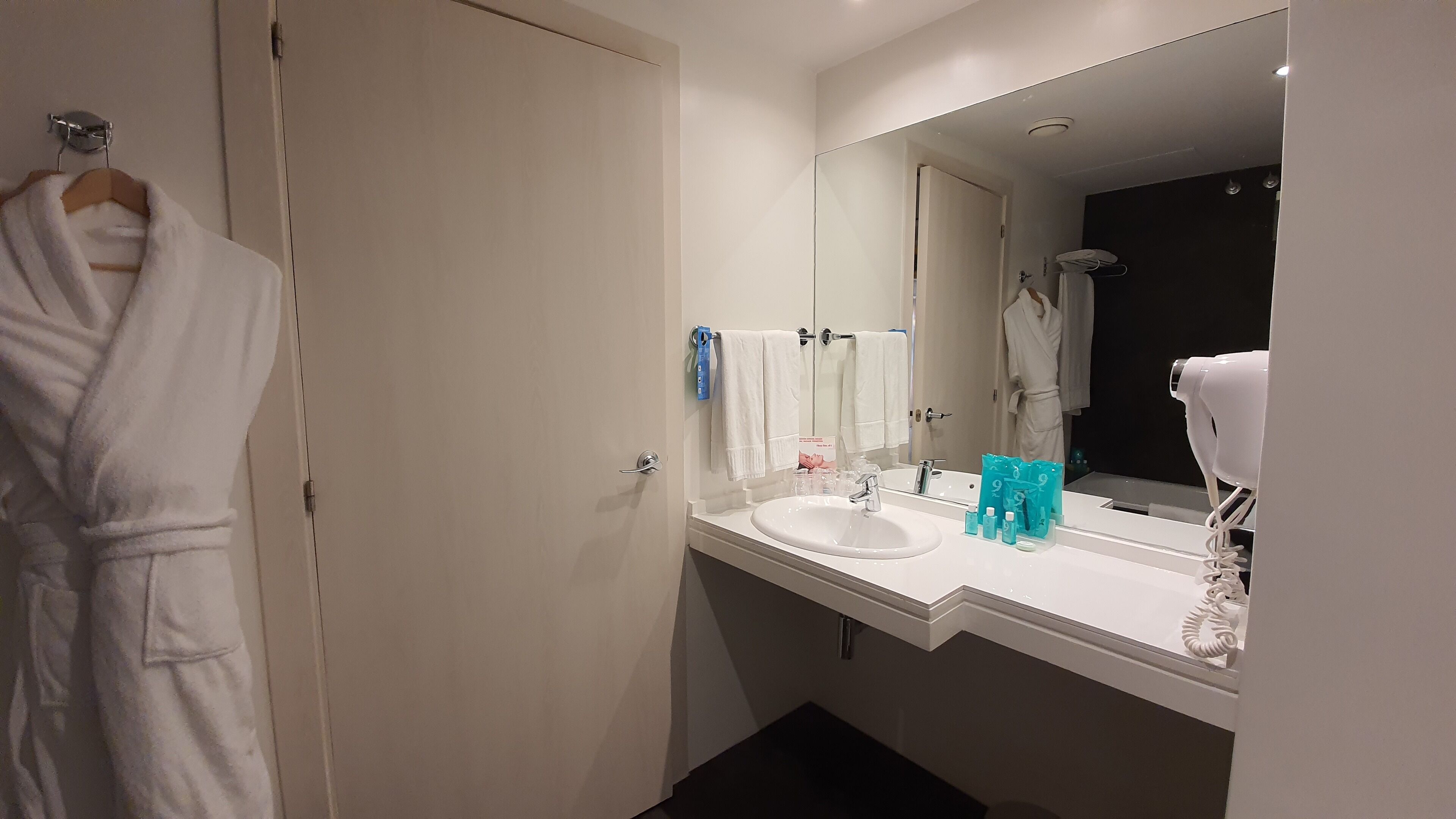 Un bagno moderno con un lavandino bianco, uno specchio grande e un accappatoio appeso a una porta.