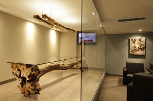 A modern reception area with a glass partition, a wooden sculptural table, and a mounted television.