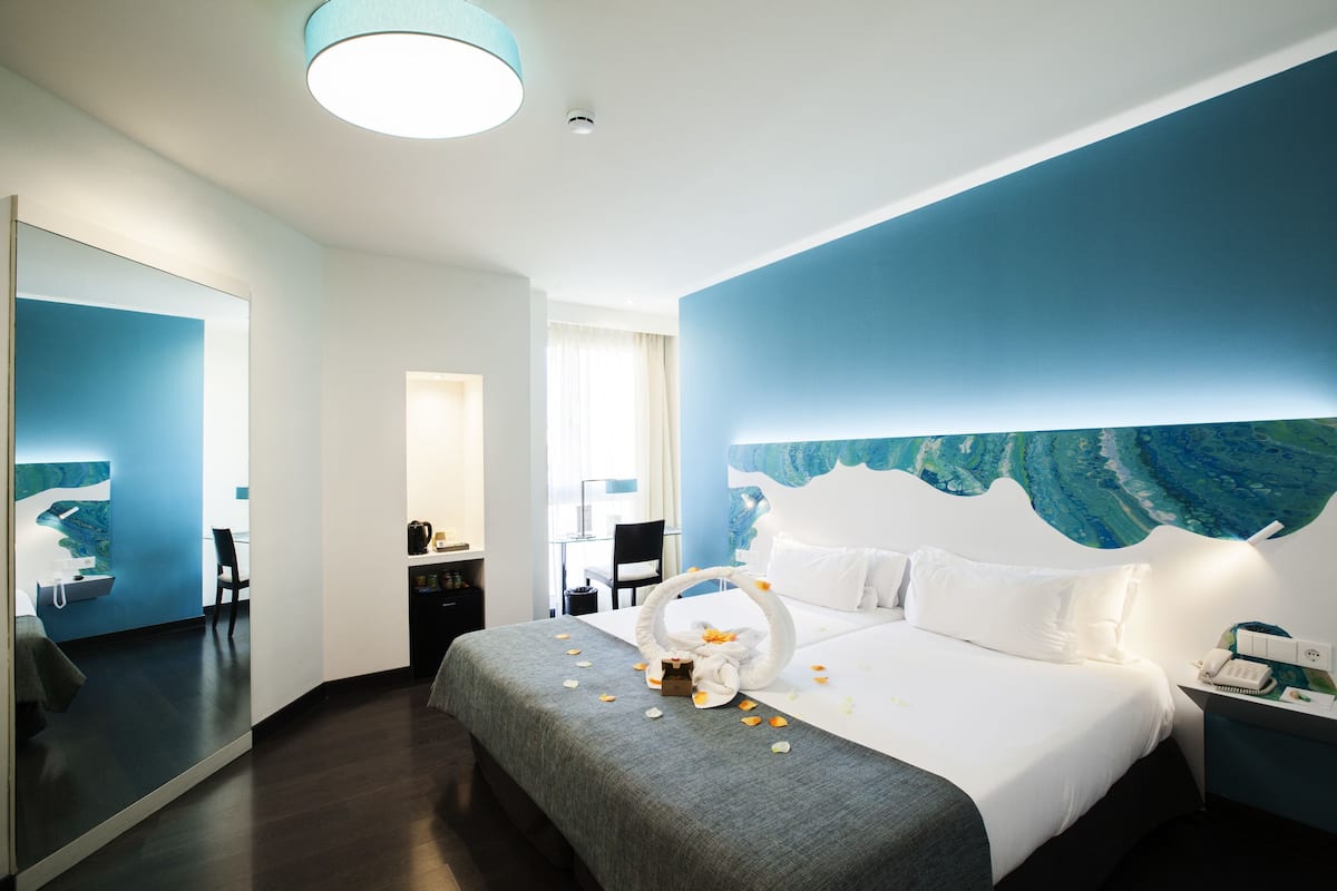 A modern hotel room with a large bed, a desk, a chair, and a bathroom.