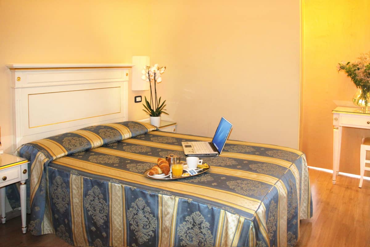Een hotelkamer met een groot bed, een laptop op het bed, een dienblad met ontbijtartikelen en een potplant.