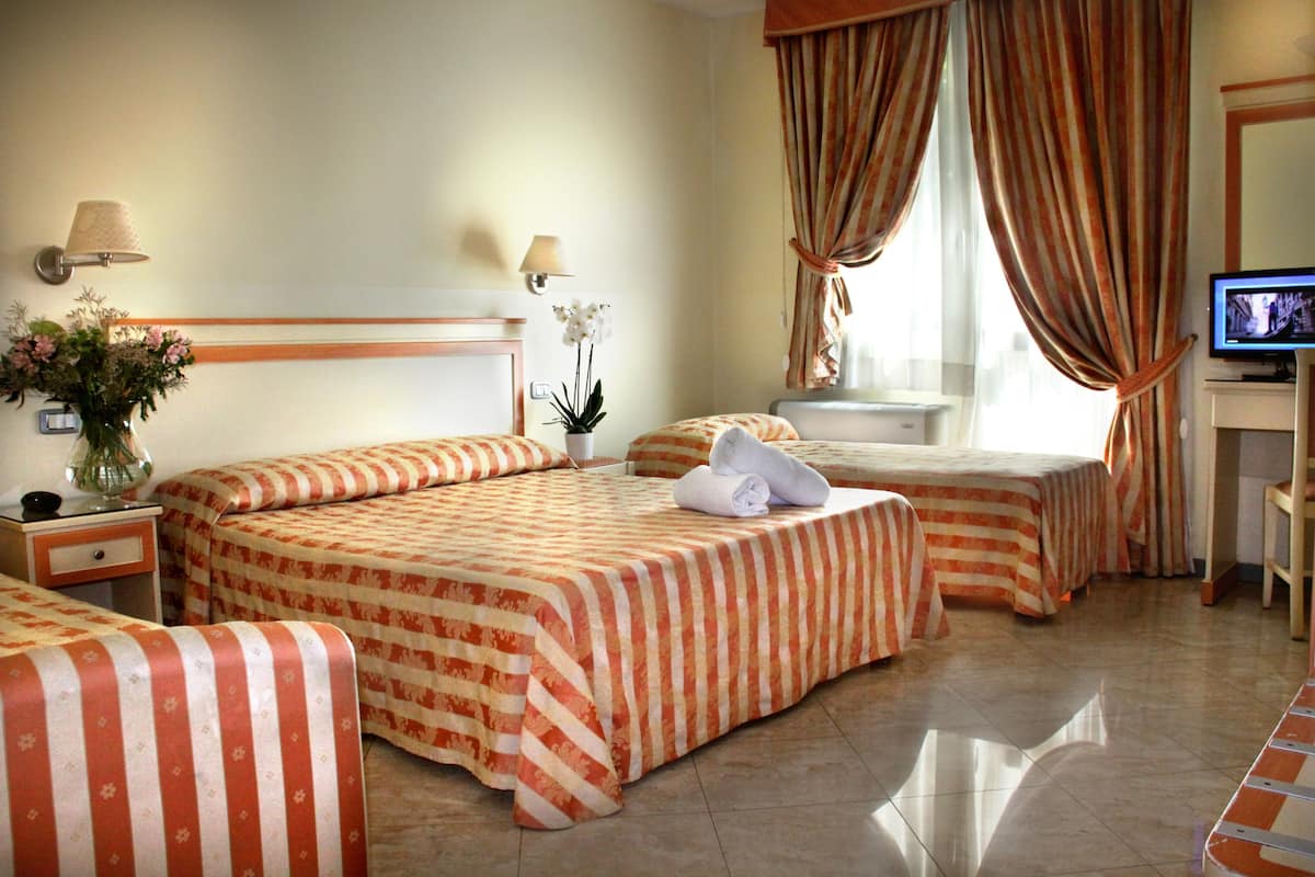 Een hotelkamer met twee bedden, een televisie, een bureau en een raam met gordijnen.