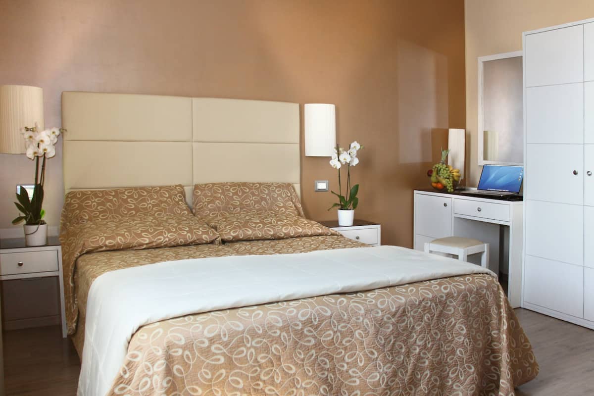 Een slaapkamer met een bed, nachtkastjes, een bureau, een stoel, een lamp, een potplant en een spiegel.