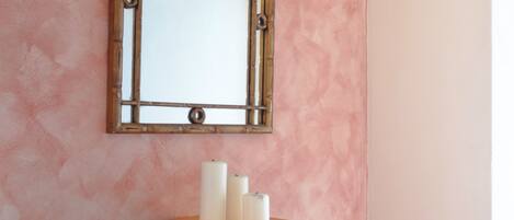 A mirror with a wooden frame on a pink textured wall, above a wooden vanity with three white candles.