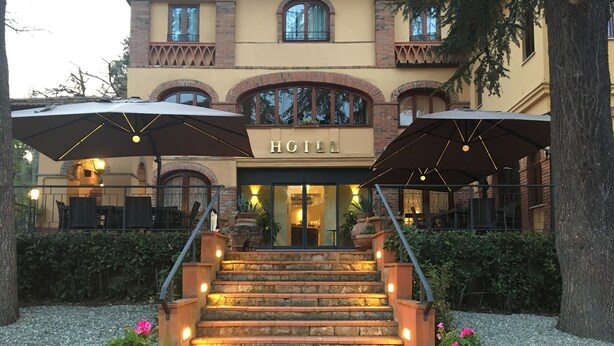 A hotel entrance with a staircase leading up to the doors, surrounded by potted plants and outdoor umbrellas. - Hotel Villa Ambrosina (Impruneta)