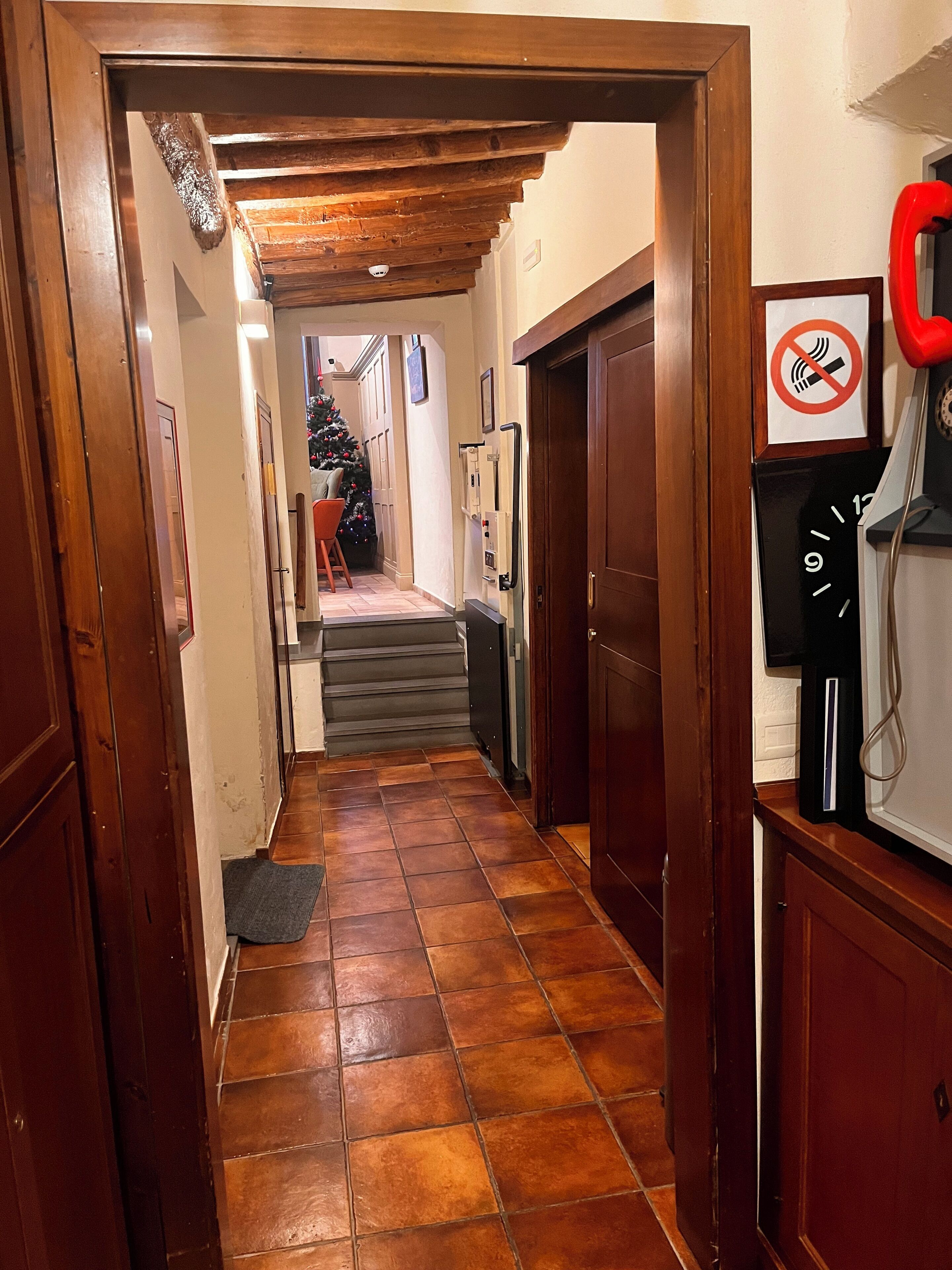 A hallway with a wooden door, a staircase, a Christmas tree, and a no-smoking sign.