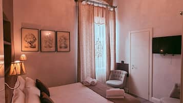 Un dormitorio con una cama grande, una araña, una silla, un televisor y obras de arte en la pared.