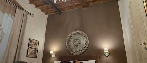 Un dormitorio con techo de madera, una araña, una cama con almohadas, dos lámparas de pared y un reloj de pared.