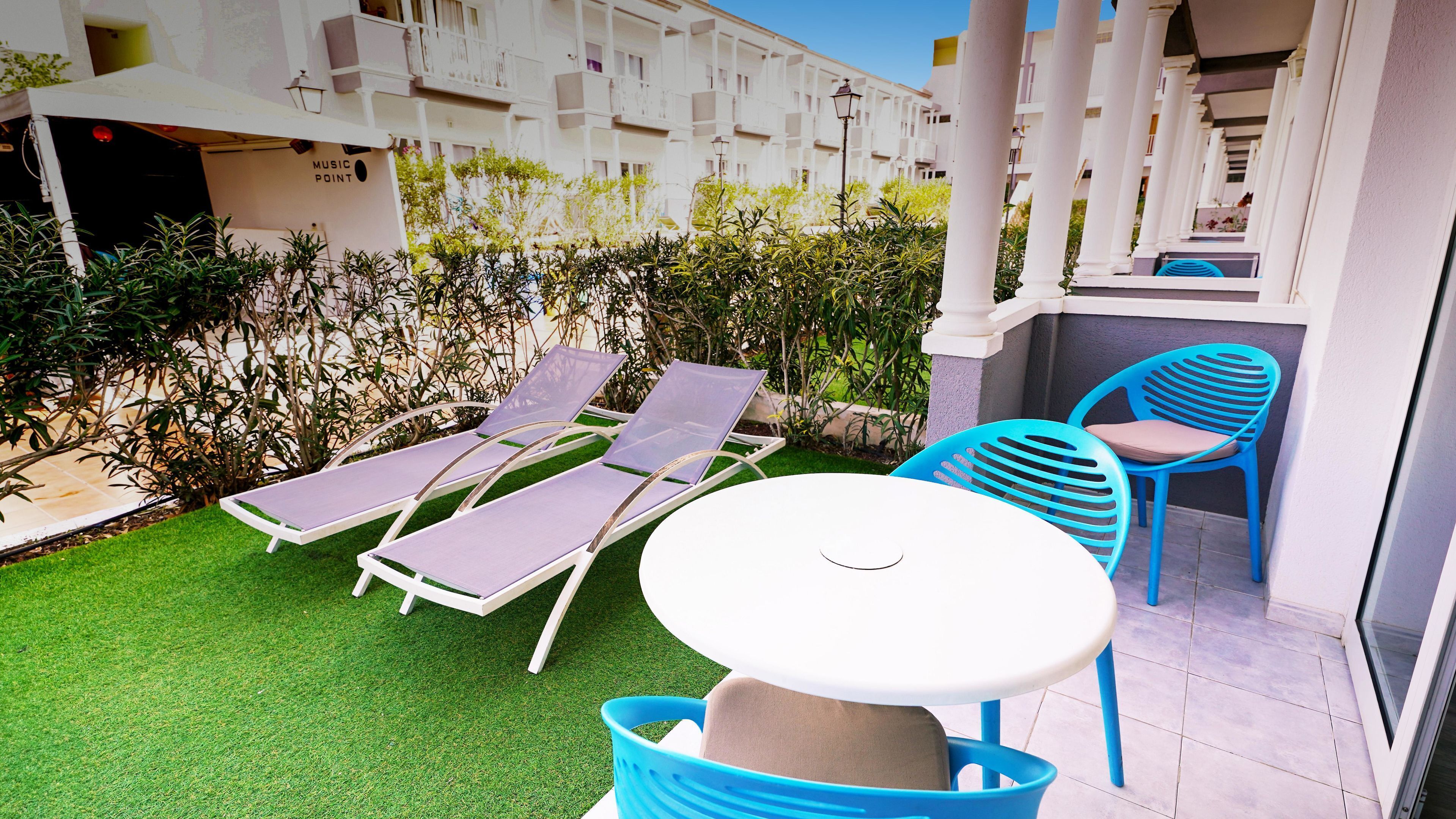 A patio with two sun loungers, a table, and blue chairs.