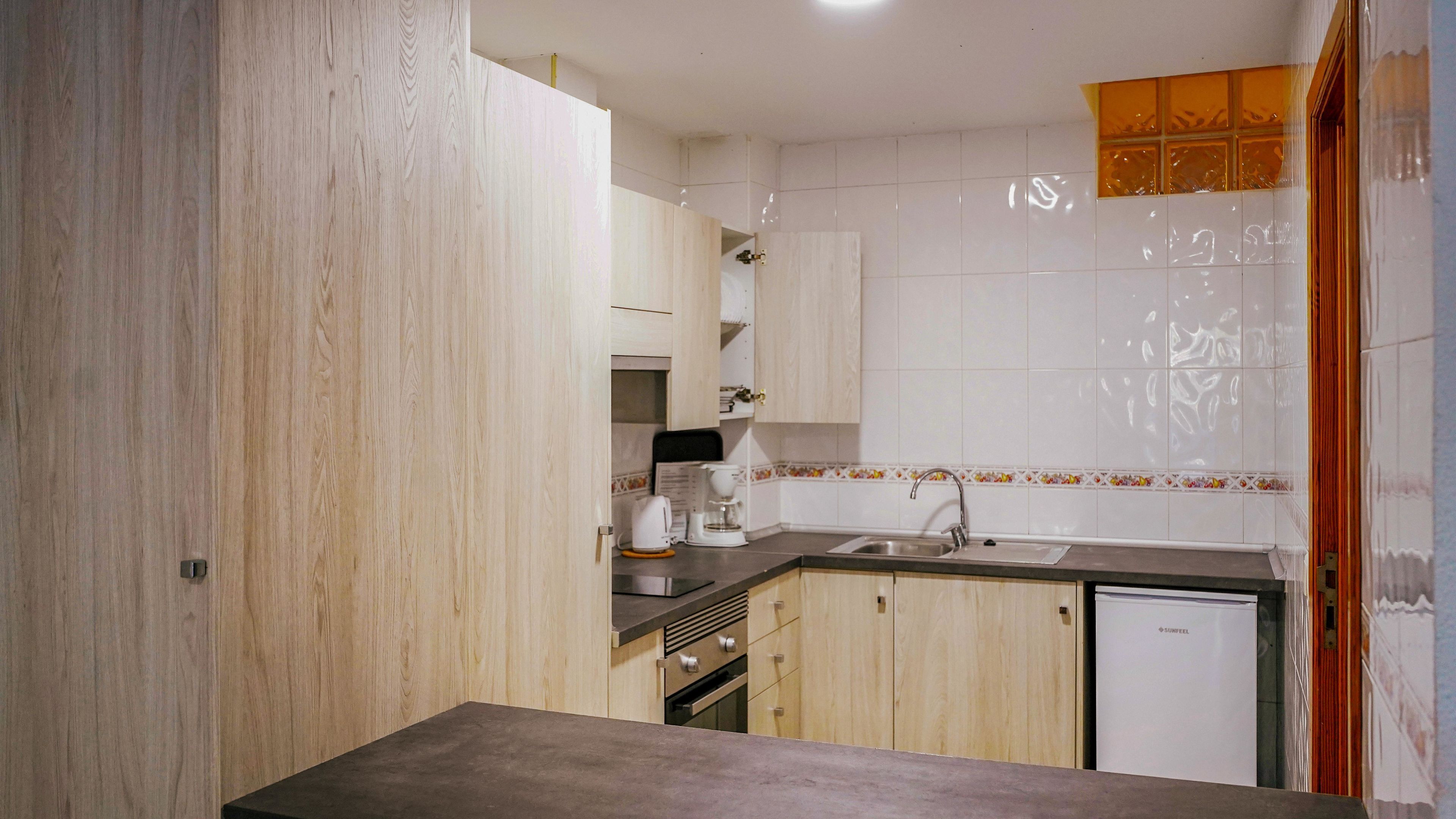 Una cocina con armarios de madera, un lavamanos, una cafetera y un refrigerador.