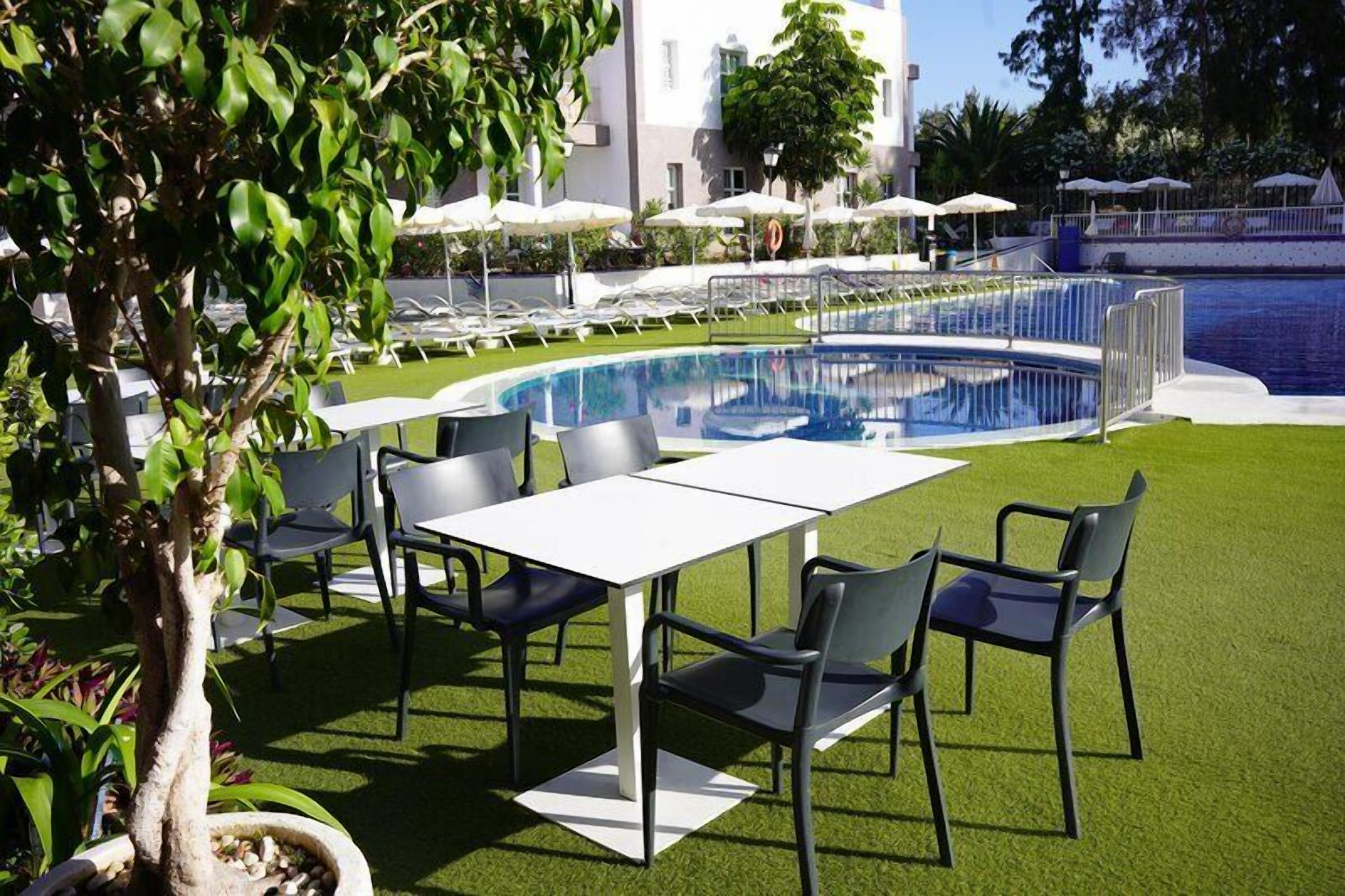 Zona junto a la piscina con una mesa y sillas, una piscina y un edificio al fondo.