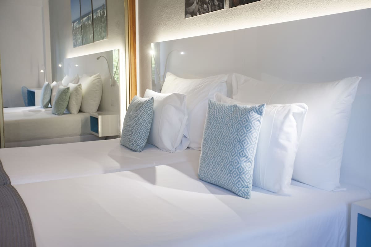 Una habitación de hotel moderna con una cama grande, varios almohadones y una mesita de noche.