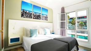 A hotel room with a bed, bedside tables, a window with a view of a pool, and a wall with a painting. - Coral Compostela Beach Golf (Arona)