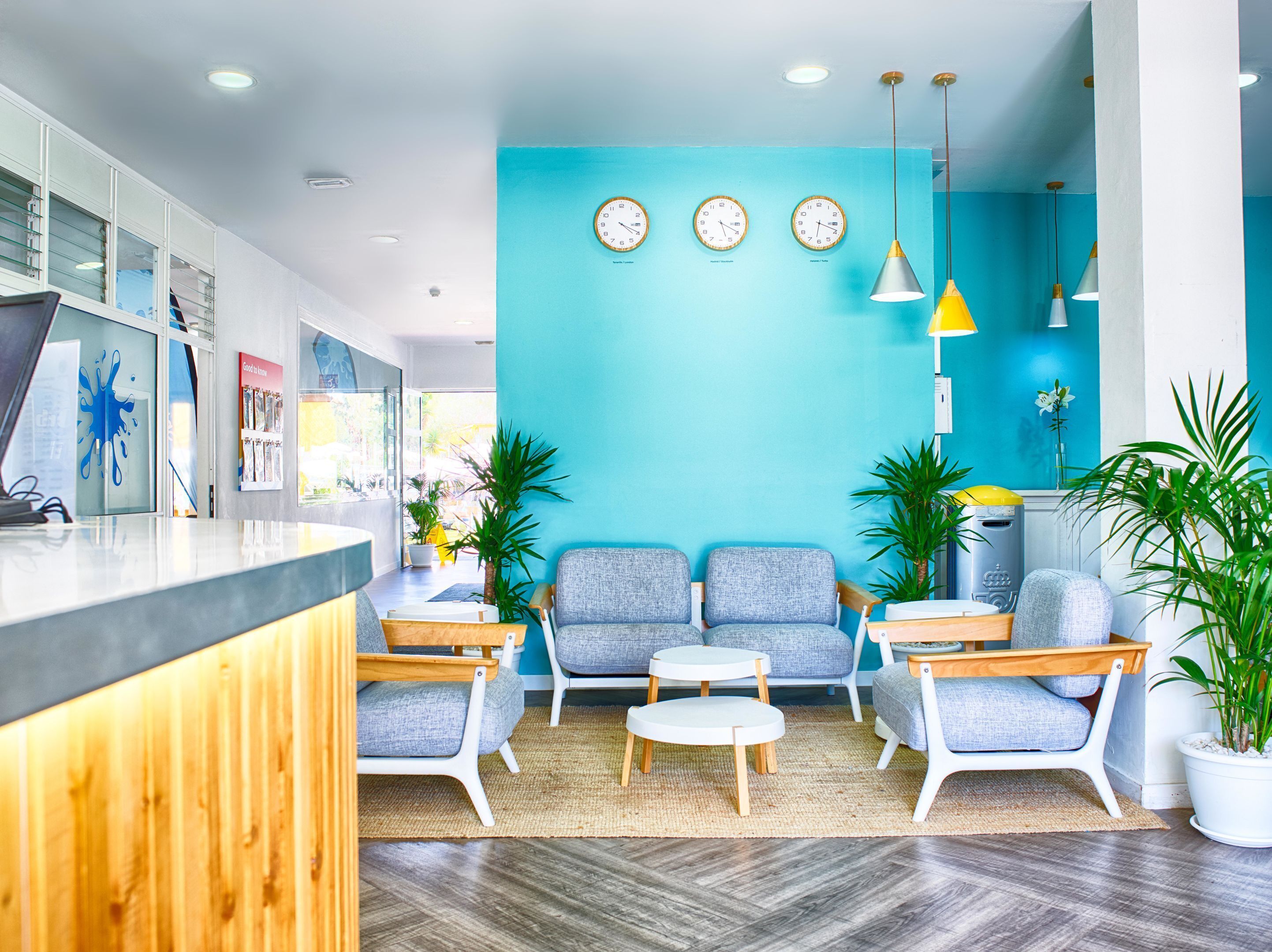 Un espace d’accueil moderne avec un mur bleu, trois horloges et des sièges disposés devant un comptoir en bois.