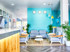 A modern reception area with a blue wall, three clocks, and seating with a wooden counter. - Coral Compostela Beach Golf (Arona)