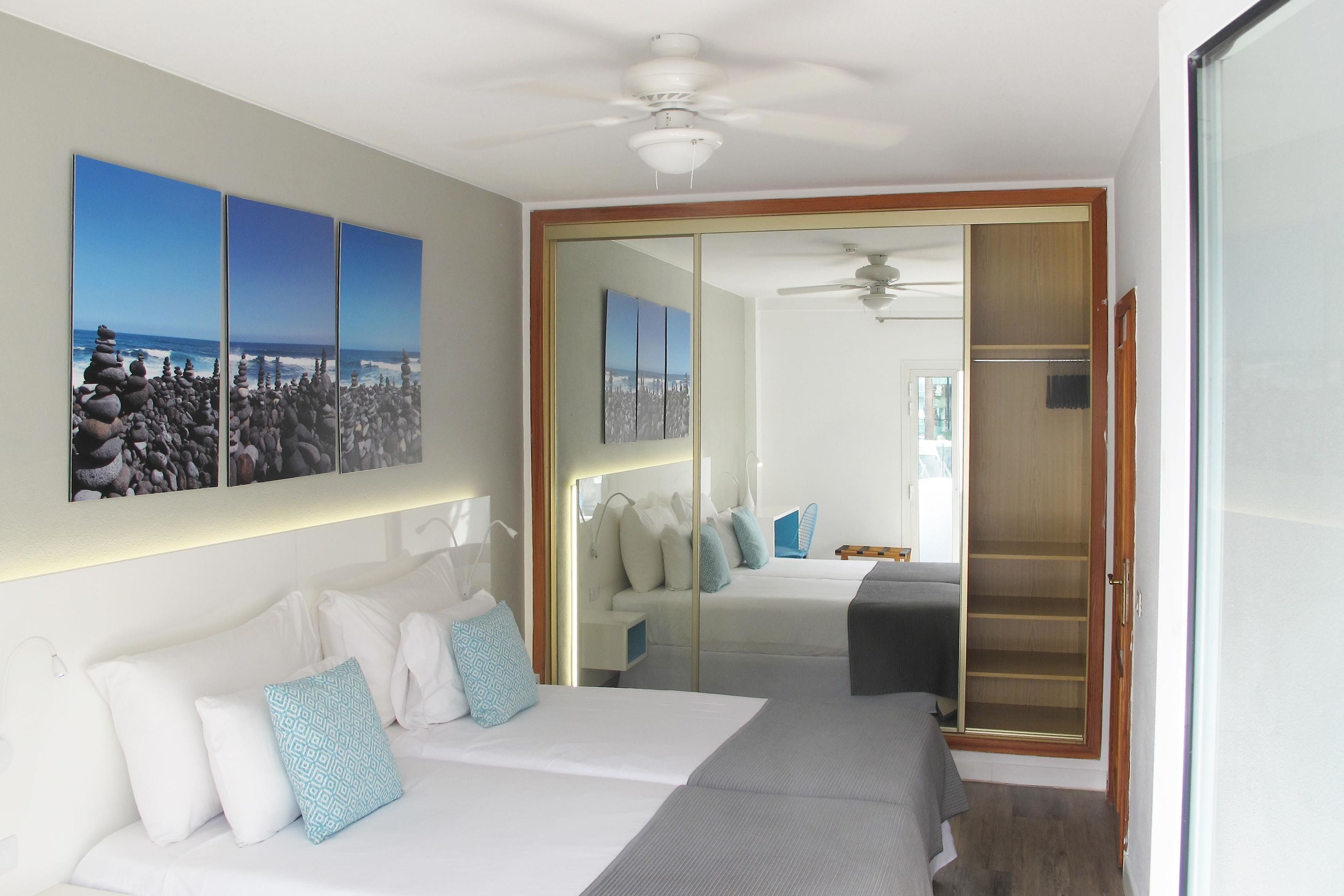 A hotel room with a bed, a seating area, a large mirror, and a view of the ocean.