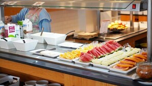 A buffet counter with various food items, including fruits, vegetables, and meats, and a person serving food in the background. - Coral Compostela Beach Golf (Arona)